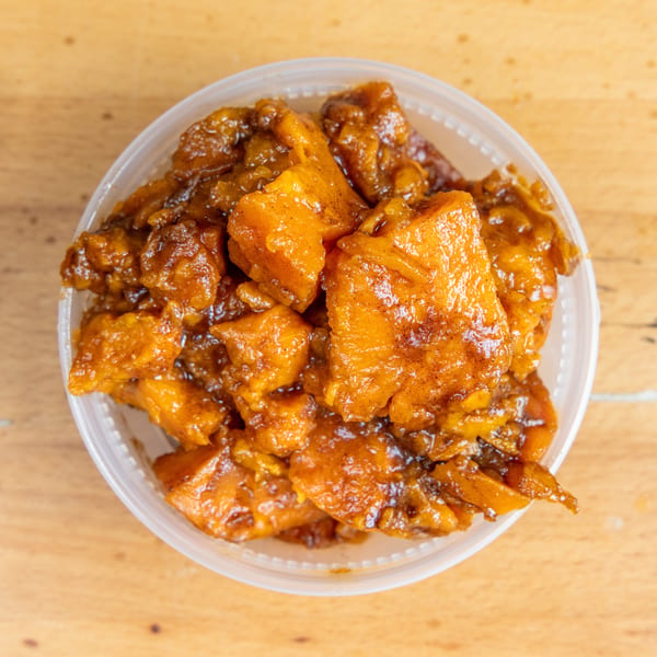 Container filled with golden-brown, sauce-coated fried food on a wooden table.