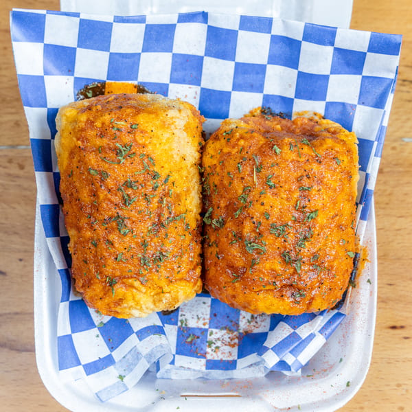Two golden, herb-seasoned fried sandwiches served in a blue-and-white checkered paper-lined tray on a wooden table.