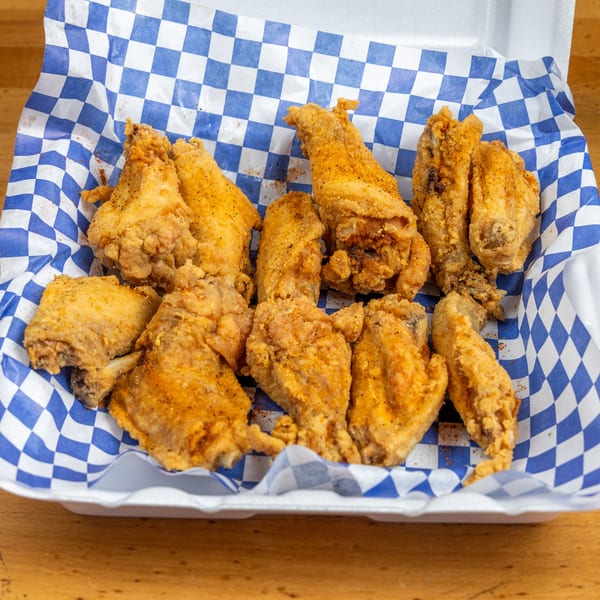 Basket of golden fried chicken pieces served on blue-and-white checkered paper atop a wooden table.