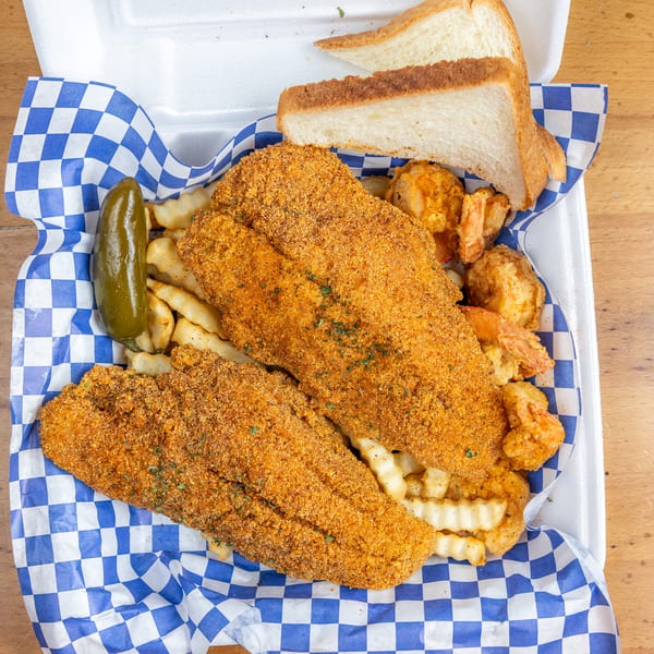 Crispy breaded fish, fried shrimp, crinkle-cut fries, pickled jalapeño, and white bread served in a blue-checkered basket.