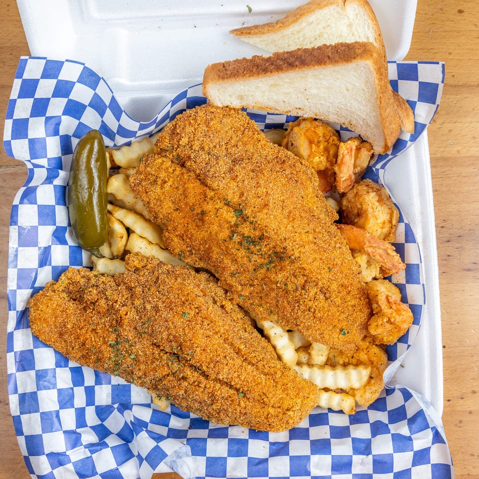 Crispy breaded fish, fried shrimp, crinkle-cut fries, pickled jalapeño, and white bread served in a blue-checkered basket.